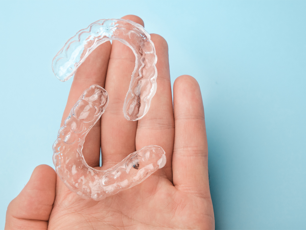 Hand holding a pair of clear plastic aligners.