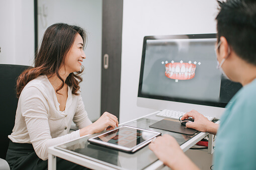 Woman seated in a dental clinic reviewing digital tooth scan results with dentist after CEREC imaging procedure.