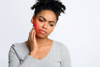 Person in light gray top touching side of face near jaw, with red highlighted area indicating dental or facial pain.